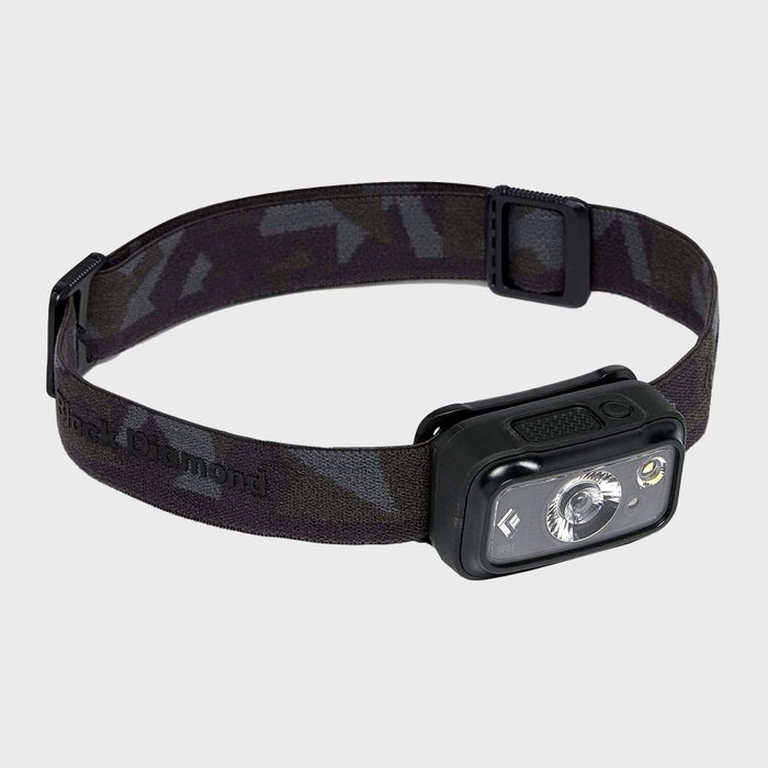 A black headlamp rests on a gray background, featuring a camouflaged adjustable strap and a front light apparatus designed for illumination during activities.