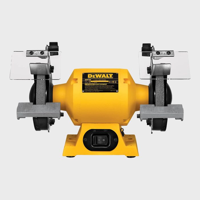 A yellow DEWALT bench grinder sits on a base, with two grinding wheels and protective shields, ready for sharpening tools in a workshop setting.