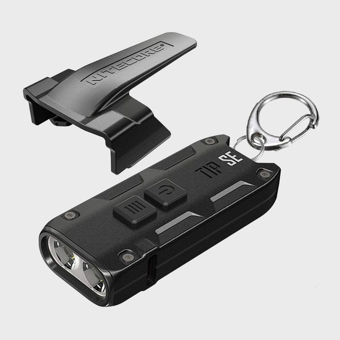 A compact black flashlight with two buttons and a keychain, alongside a detachable clip, rests on a light gray background.