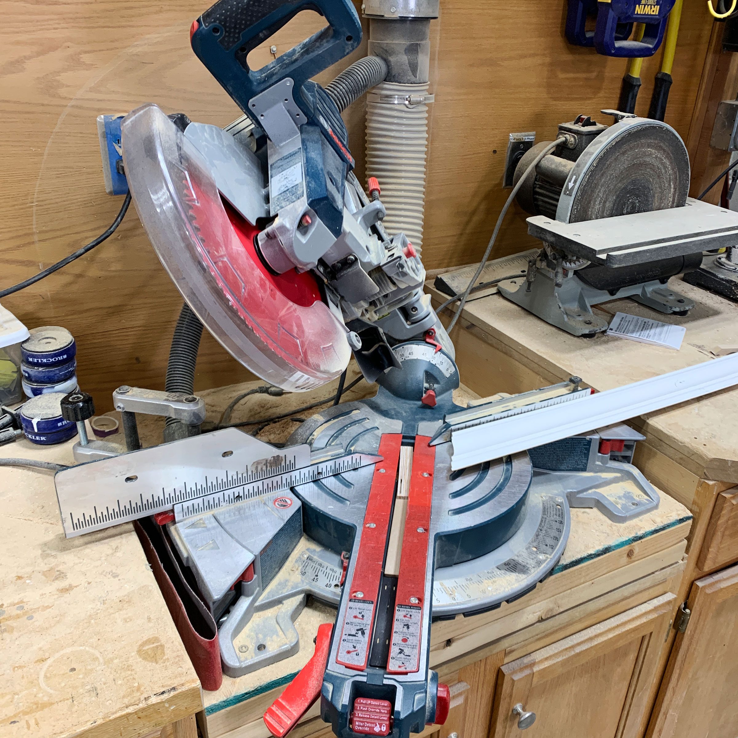 A miter saw sits on a workbench, angled, ready to cut a piece of trim while surrounded by wood shavings and other tools.