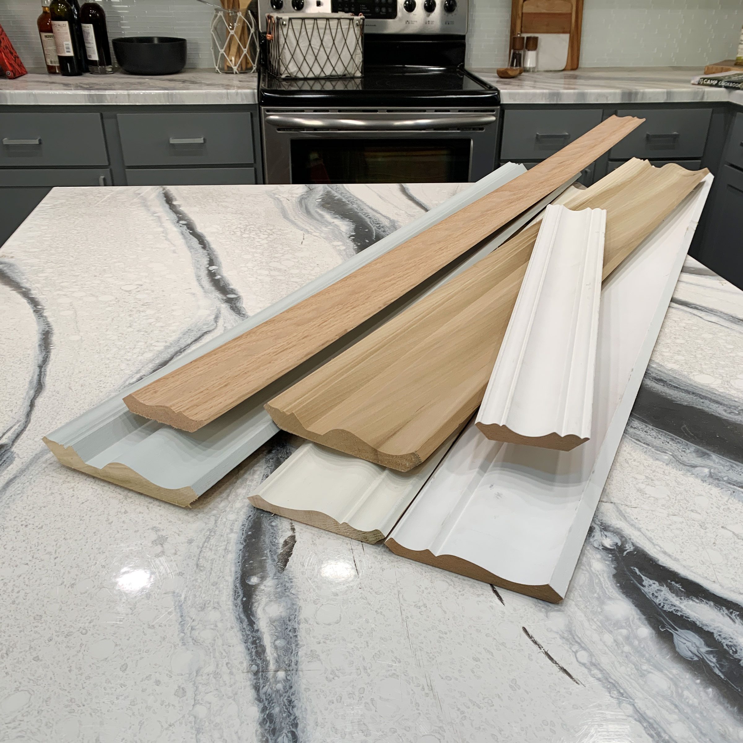 Wood and plastic molding pieces lie on a marbled countertop, while a kitchen background features an oven and storage containers.