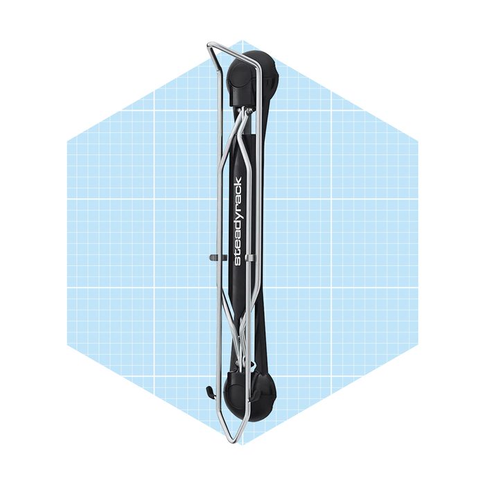 A black, foldable bike rack stands vertically against a light blue, grid-patterned background, showcasing its streamlined design and functionality for storing bicycles.