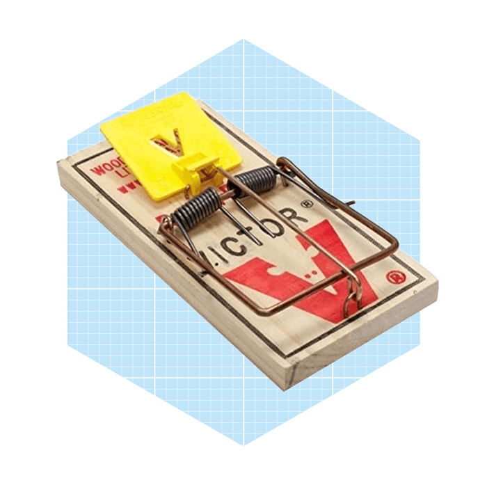 A wooden mouse trap with a yellow trigger is set, designed to capture rodents, placed against a light blue geometric background.