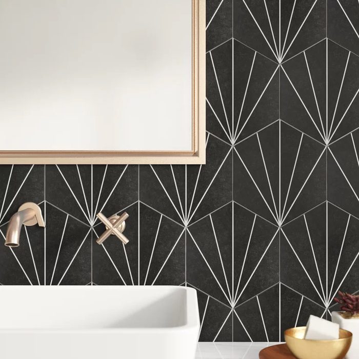 A white bathtub sits against black tiled walls with white geometric patterns, featuring a faucet and a control knob, alongside a mirror and decorative bowls.