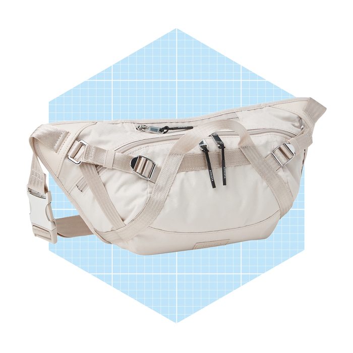 A light-colored, stylish bag rests at an angle, showcasing multiple zippered pockets and adjustable straps against a soft blue, grid-patterned background.