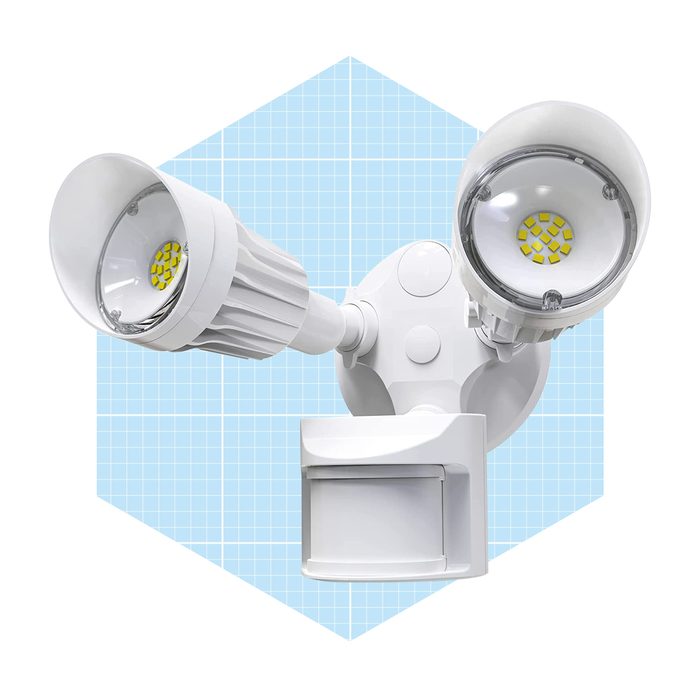 A dual-headed motion sensor light illuminates, mounted on a white base against a light blue grid background, designed for outdoor security.