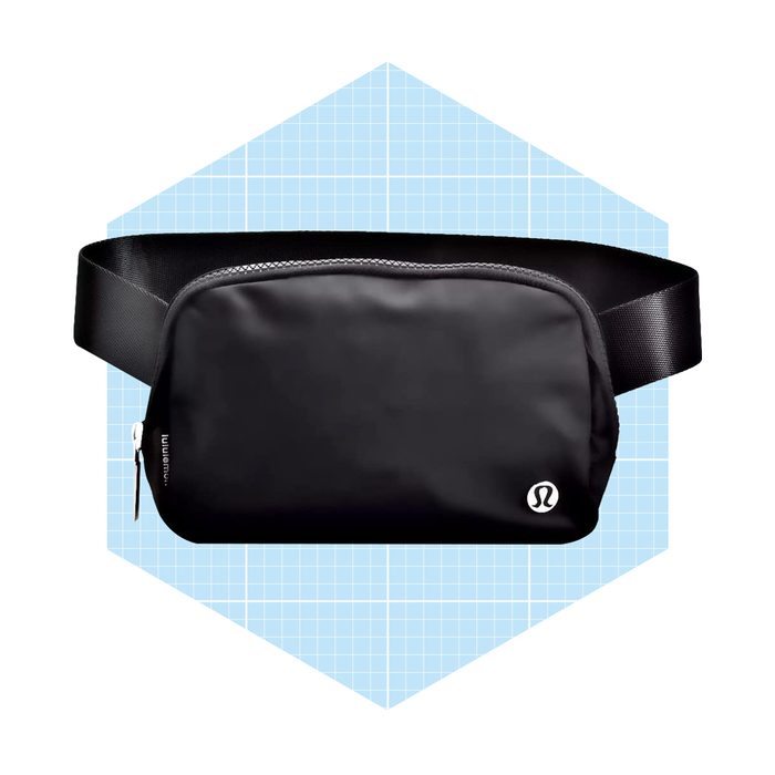 A black waist bag rests on a light blue, grid-patterned background, showcasing a sleek design with a zipper and an adjustable strap.