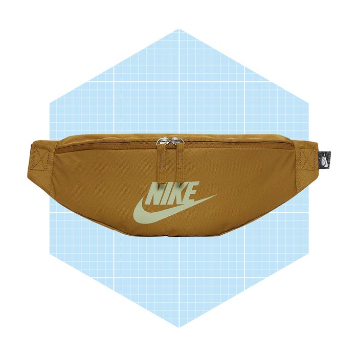 A brown fanny pack with a Nike logo rests on a light blue grid-patterned background, showcasing its sleek design and dual zipper compartments.