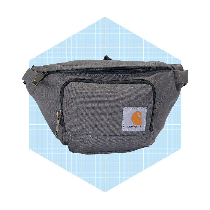 A gray fanny pack features zippers and a front pocket, displayed against a light blue, grid-patterned background, showcasing its functionality and style.