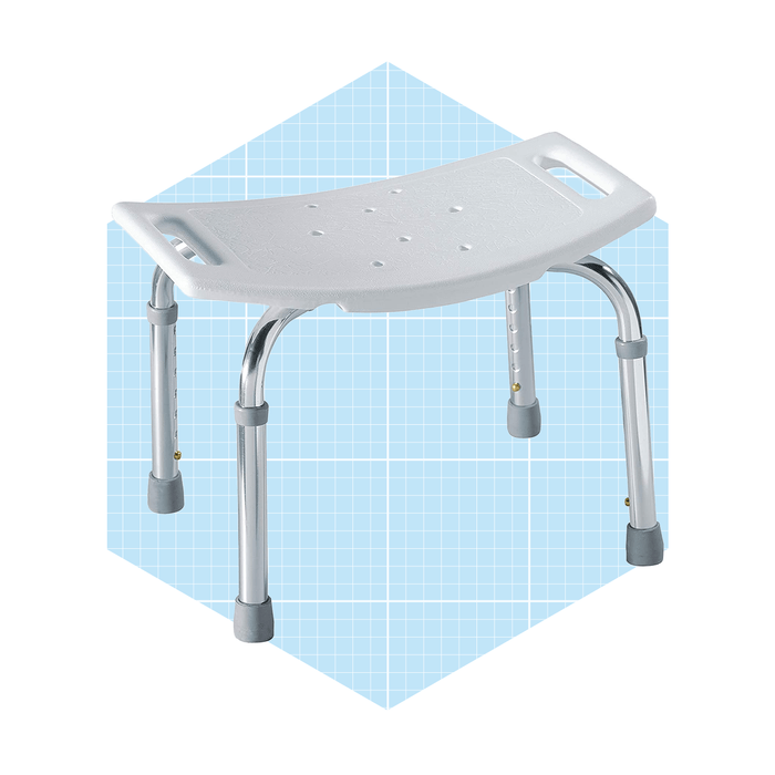 A white shower stool with a textured seat and chrome legs stands on a light blue grid background, designed for stability and support in wet environments.