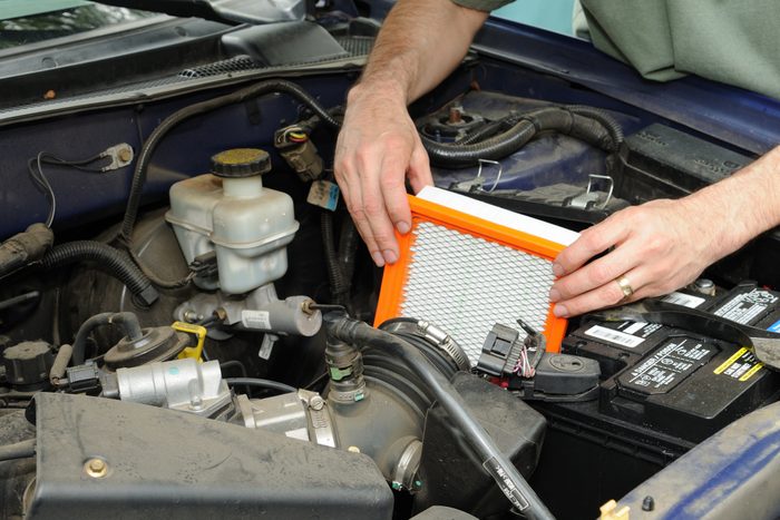 A person installs an orange-framed air filter in a vehicle's engine compartment, surrounded by various automotive components and a car battery.
