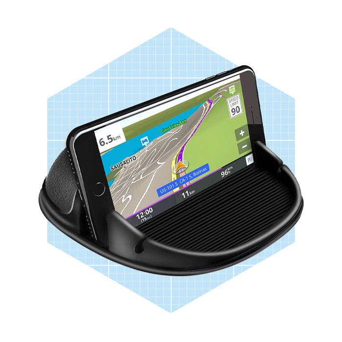 A smartphone is displayed in a black dashboard mount, showing a navigation map with driving directions, surrounded by a light blue hexagonal background.