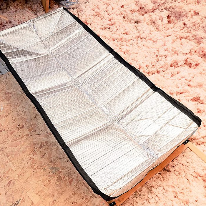 A reflective sleeping pad lies flat on a textured surface, providing insulation in a cozy indoor environment with soft, light-colored flooring.