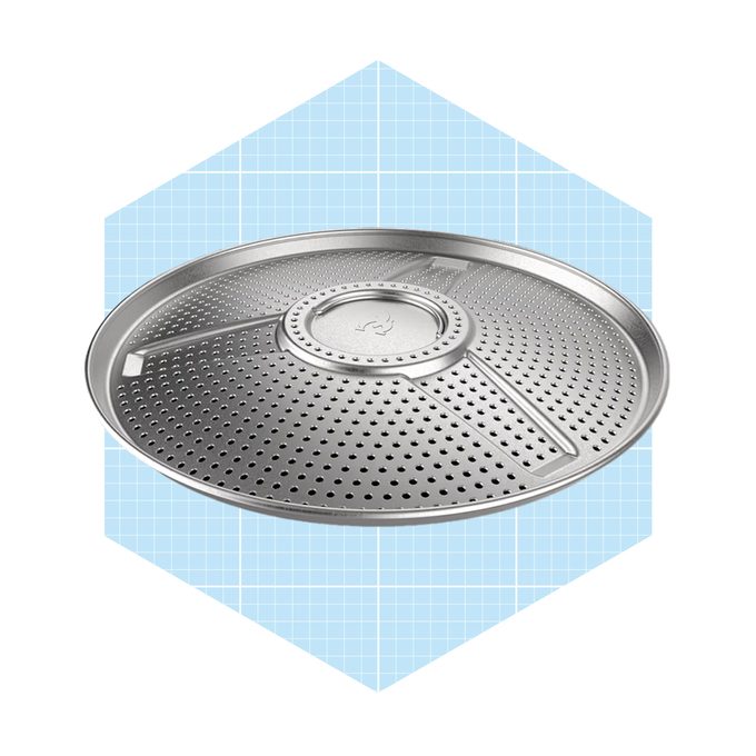 A round, perforated metal baking tray rests prominently against a light blue grid background, designed for even cooking and draining.