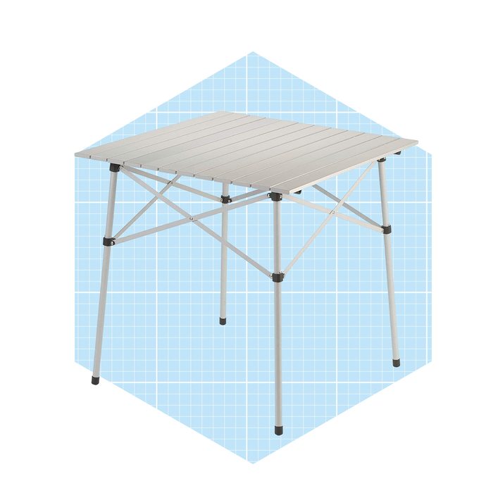 A lightweight folding table stands upright, featuring a slatted aluminum top and metal legs on a light blue grid background.