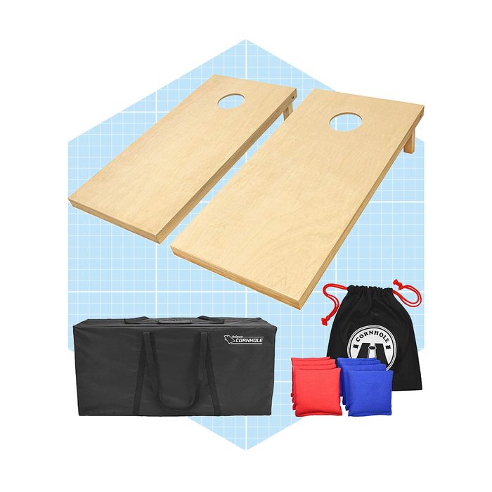 Two wooden cornhole boards are positioned parallel, with a carrying case and red and blue bean bags in front, set against a light blue grid background.
