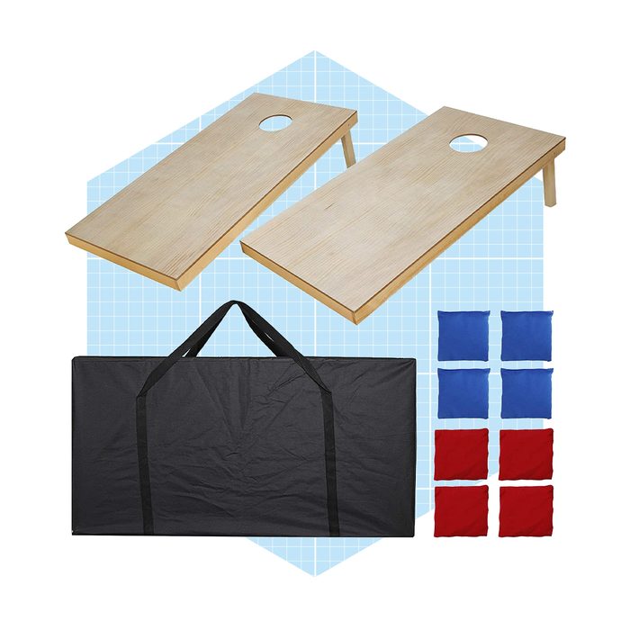 Two wooden cornhole boards are placed upright, with a black carrying bag and eight colored bean bags (four red, four blue) displayed on a grid background.