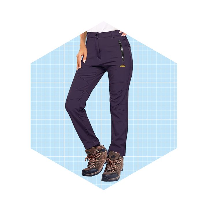 Dark purple hiking pants are worn by a person standing, with one hand on the hip, against a light blue grid background.