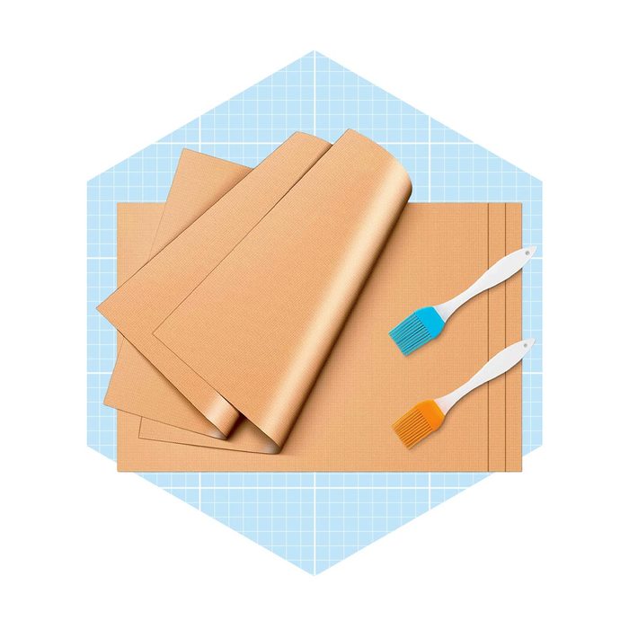 Brown crafting sheets lie stacked, while two silicone brushes, one blue and one orange, rest beside them on a light blue grid background.