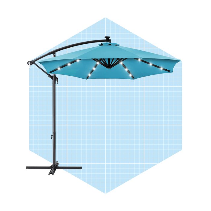 A teal patio umbrella stands supported by a black base, illuminated with lights, set against a light blue grid background.