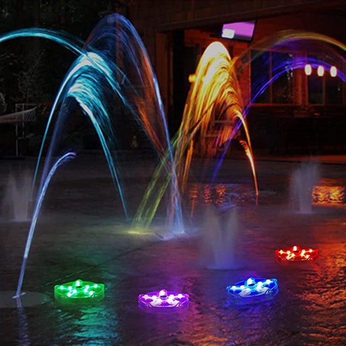 Colorful water fountains spray streams of light in various arcs, while illuminated floating devices rest on the surface of a dark pool.