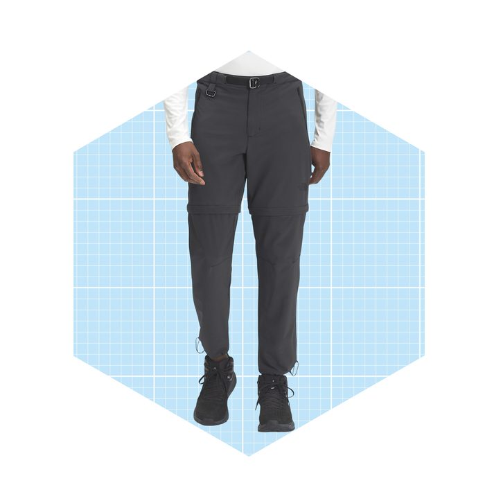 Dark cargo pants with zippers are worn by a person standing against a light blue grid background. The person is ready for outdoor activities.