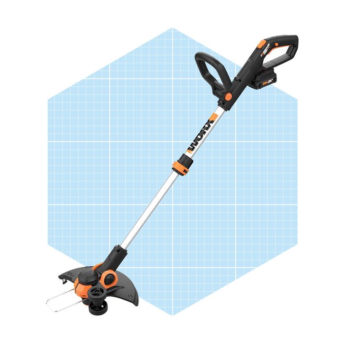 A battery-operated string trimmer stands vertically, with an orange and black design, displayed on a light blue grid background, ready for grass cutting tasks.