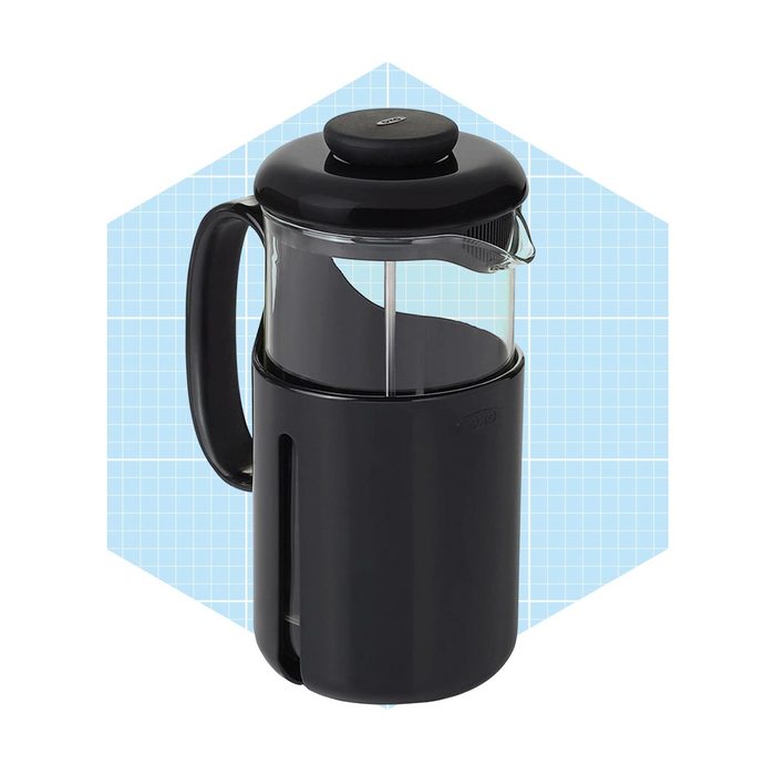 A black French press stands upright, used for brewing coffee, against a light blue grid background, showcasing its design and functionality.