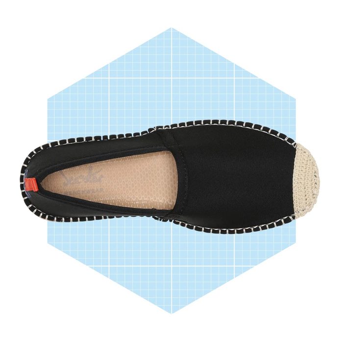 A black slip-on shoe displays a woven, light-colored toe cap, centered against a light blue grid background, emphasizing its design and features.