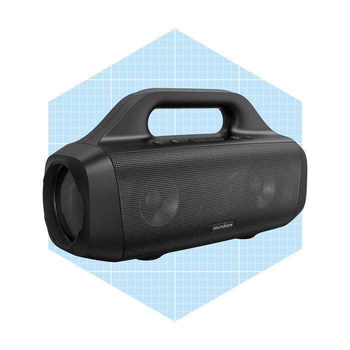 A black portable speaker plays music, positioned against a light blue grid background, featuring a handle and control buttons on top.