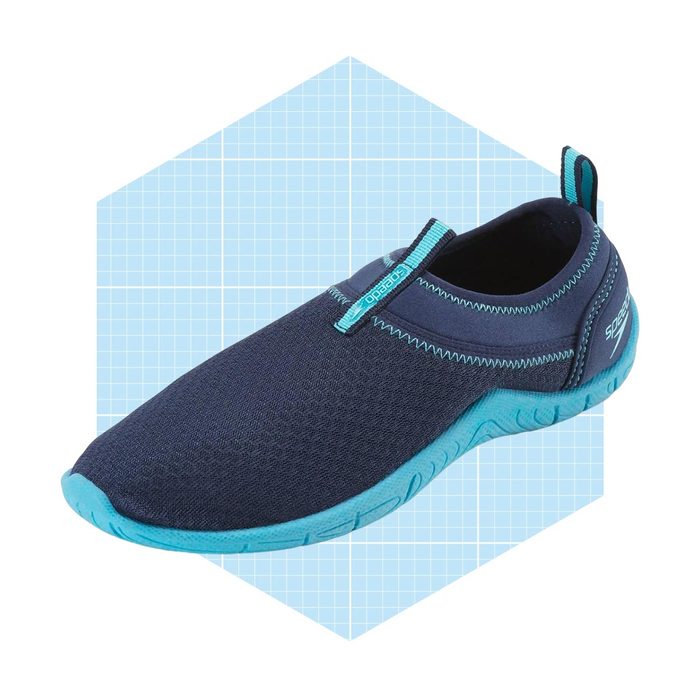 A navy water shoe is displayed, positioned at an angle on a light blue grid background, showcasing its flexible design and contrasting aqua sole.