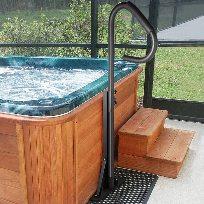 A grab bar stands next to a hot tub, helping users enter and exit safely, set in a screened area surrounded by greenery.
