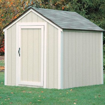 A storage shed stands on green grass, featuring a sloped roof, vertical siding, and a closed door with a decorative handle. Trees are in the background.