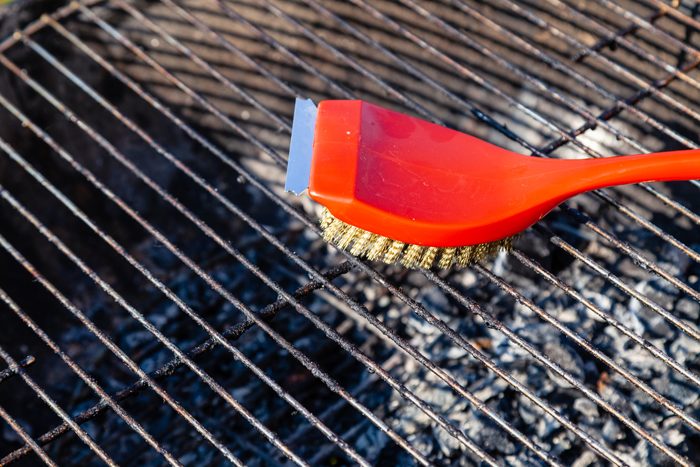 Close-up of a red brush with golden bristles and a scraper for cleaning a barbecue grill grate. The concept of cleaning after lunch in open air, picnic, barbecue, lunch