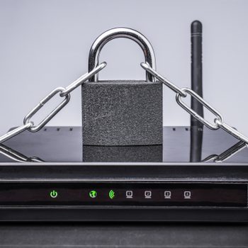 A black router is secured with a padlock and chain, positioned on a reflective surface, with green indicator lights illuminated.