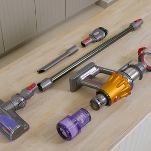 A disassembled cordless vacuum cleaner on a wooden surface. Visible parts include the main body with a yellow accent, a long tube, a roller attachment, and several smaller components.